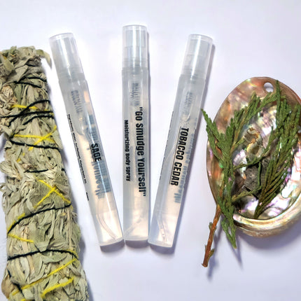 Three small perfume sprays are shown against a white background. There is real sage and cedar to the left and right of the three bottles.