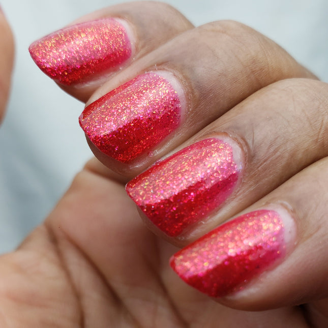 Close-up of a hand with red glittery nail polish on a blurred background