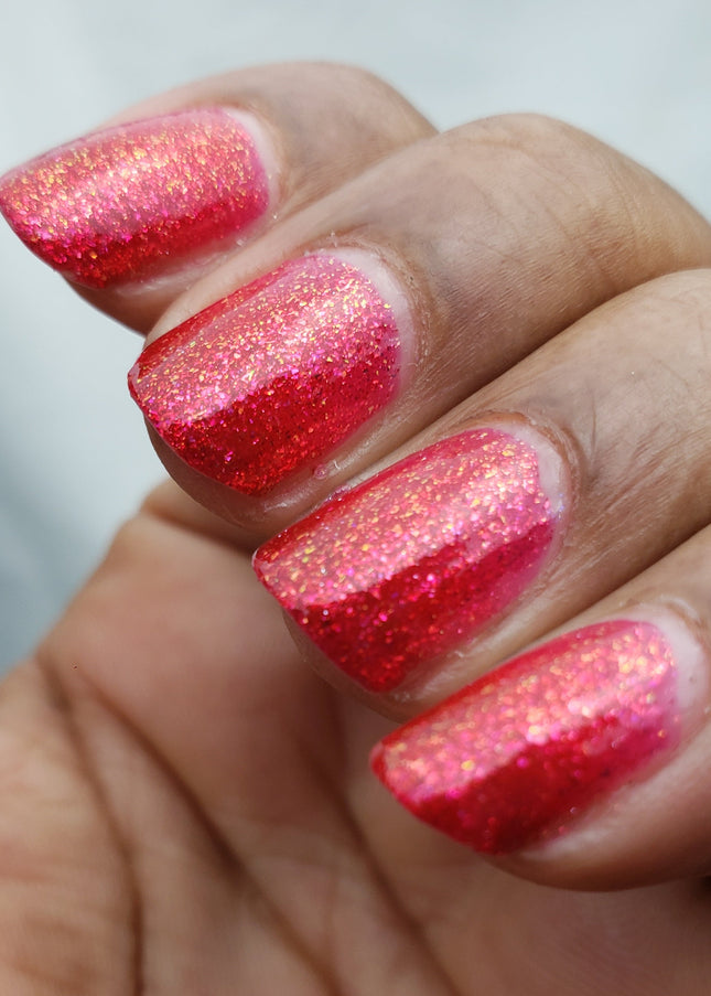 Close-up of a hand with red glittery nail polish on a blurred background