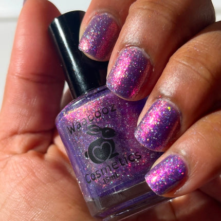 Hand holding a bottle of purple glittery nail polish with matching nails.