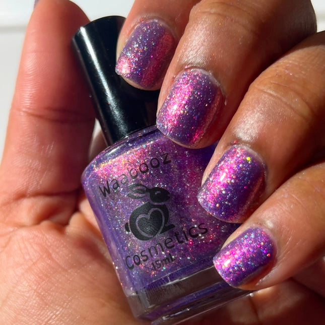 Hand holding a bottle of purple glittery nail polish with matching nails.