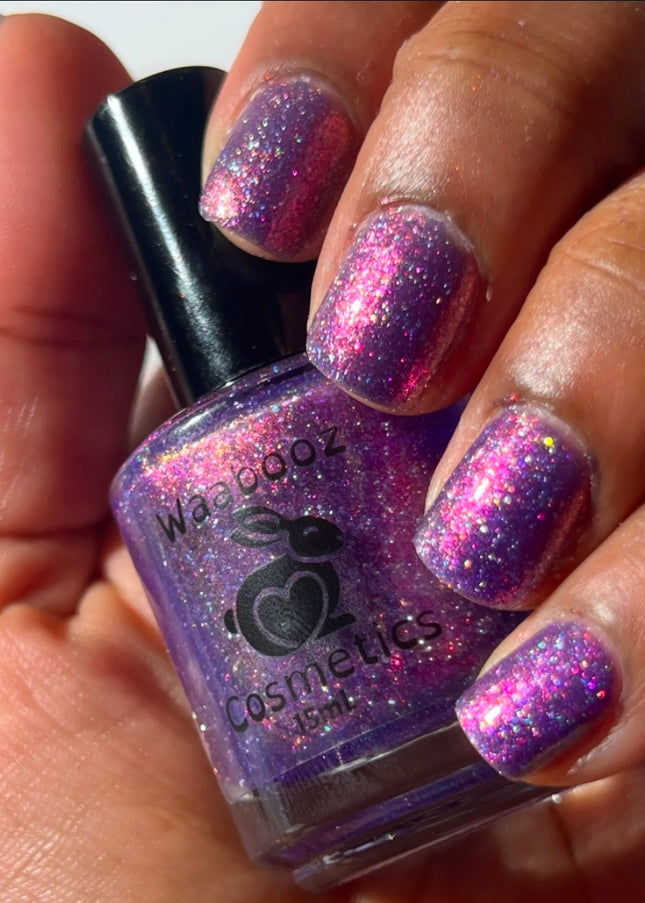 Hand holding a bottle of purple glittery nail polish with matching nails.